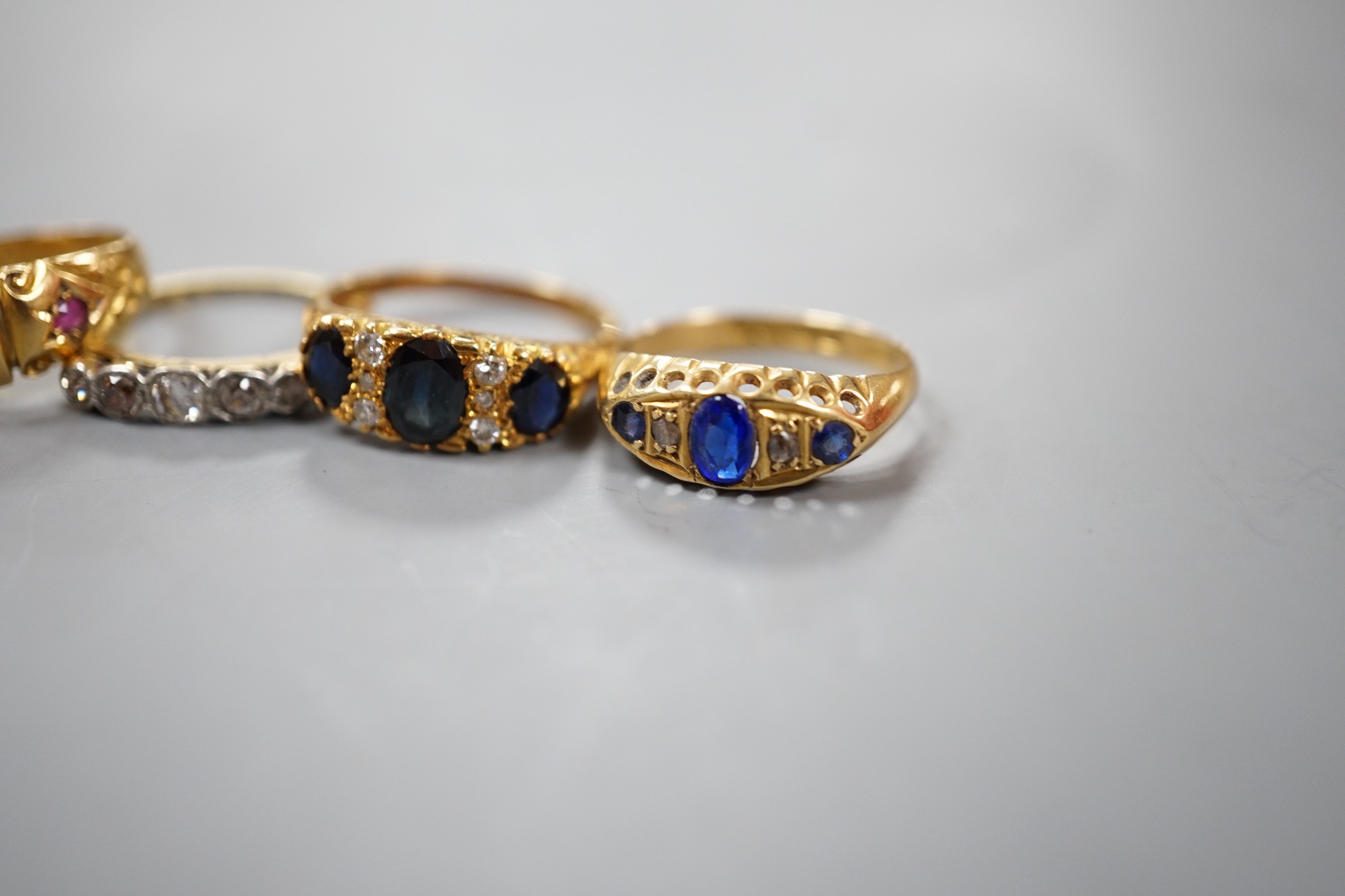 Three early 20th century 18ct and gem set half hoop rings, including ruby and diamond chip, five stone diamond, blue paste and blue stone doublet and diamond chip and a modern 18ct gold sapphire and diamond ring, gross w